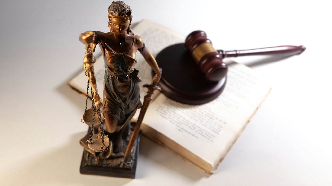 Statue of justice, gavel, and open book on table.
