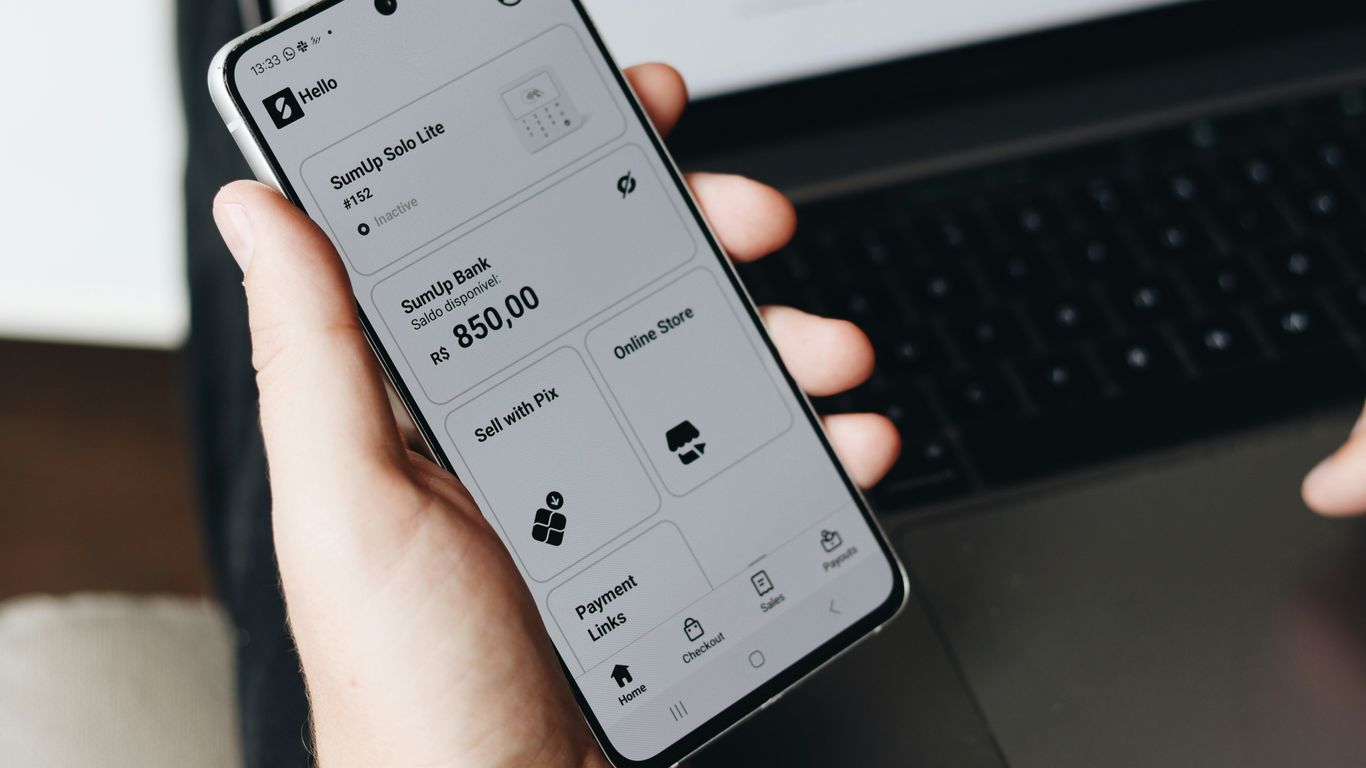 A person holding a cell phone in front of a laptop