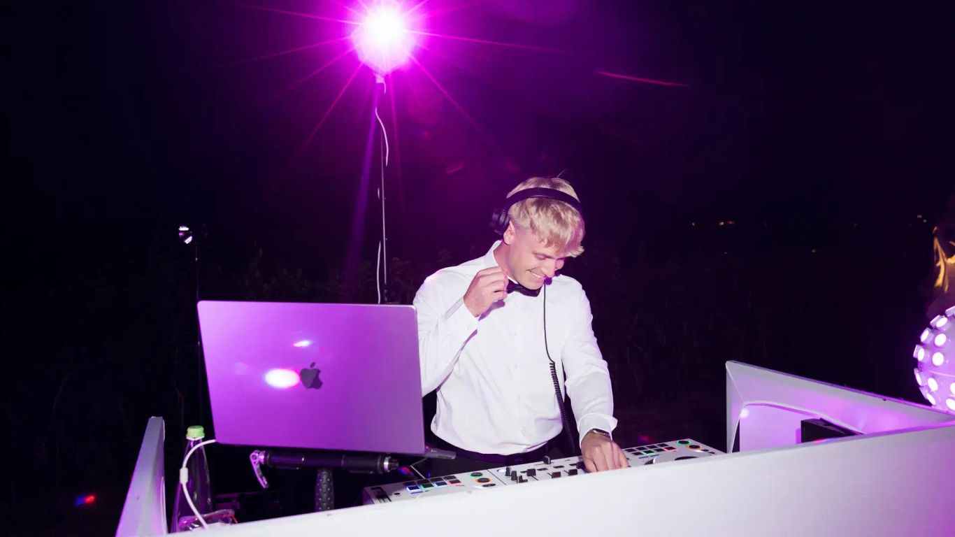 DJ performing at night with purple lighting and equipment.