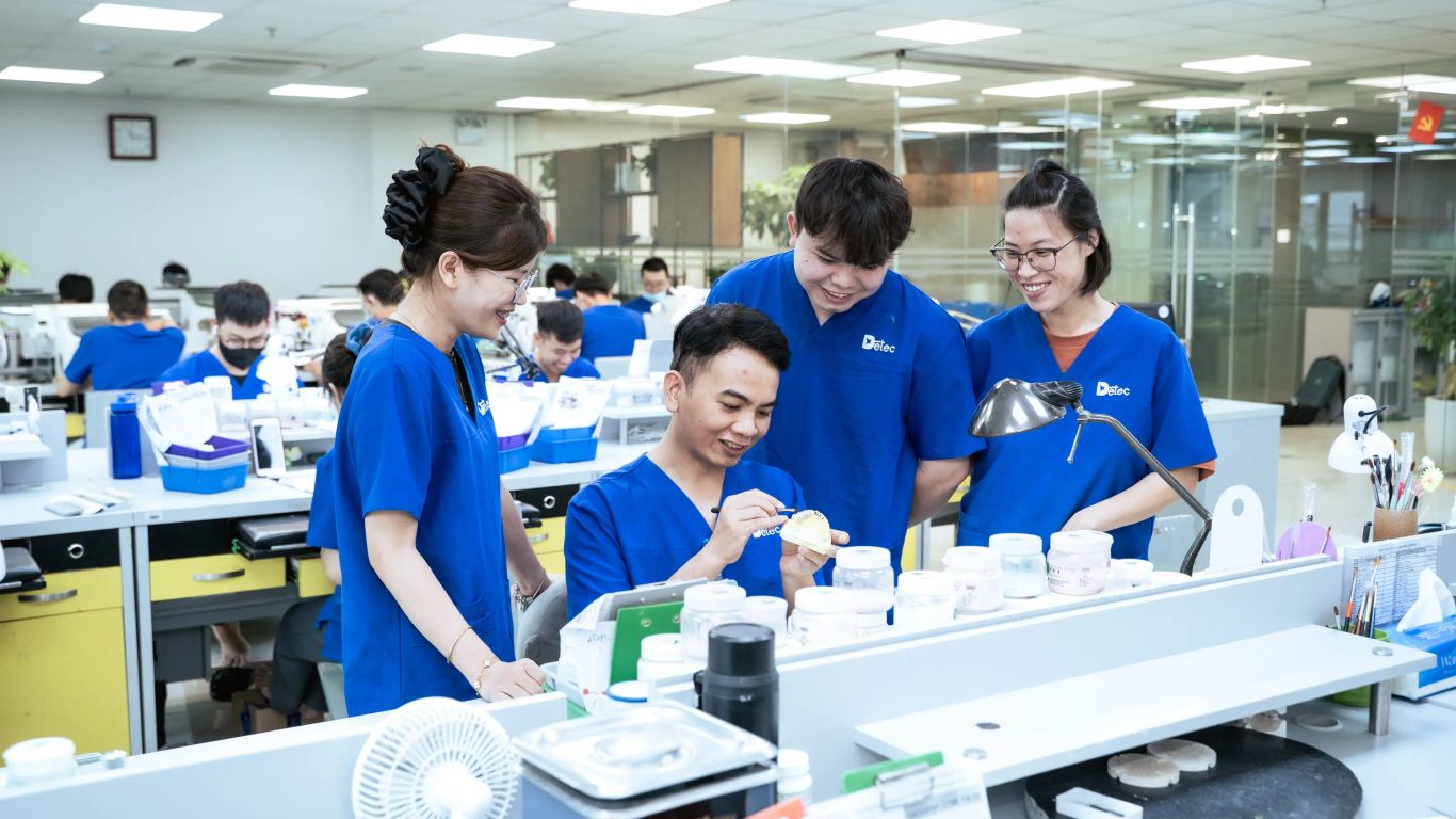 People in blue uniforms working in a dental laboratory with tools and materials.