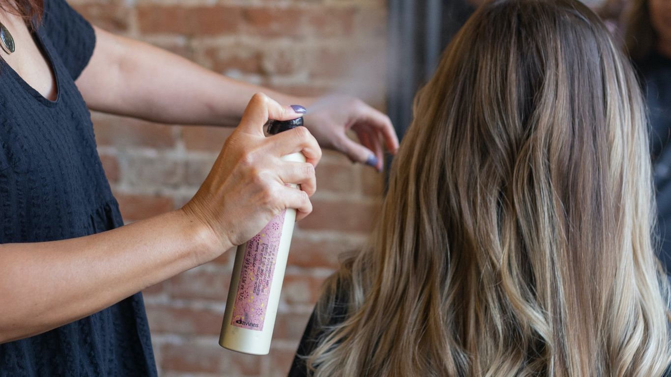 Stylist applying hairspray to client's hair in salon.
