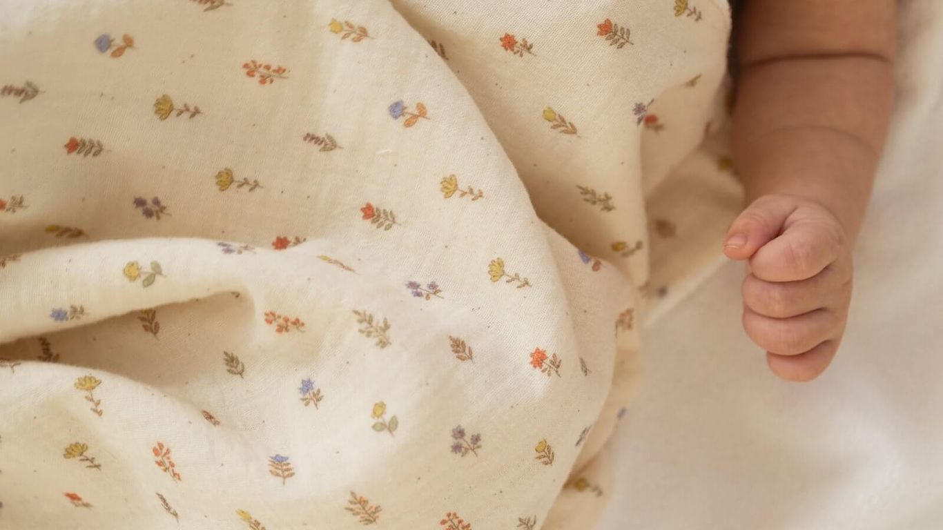 A baby wrapped in a floral blanket, with a hand visible.
