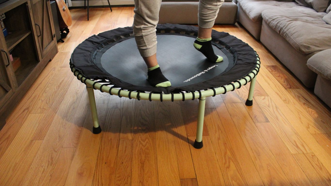 Person standing on mini trampoline in living room, wearing socks.
