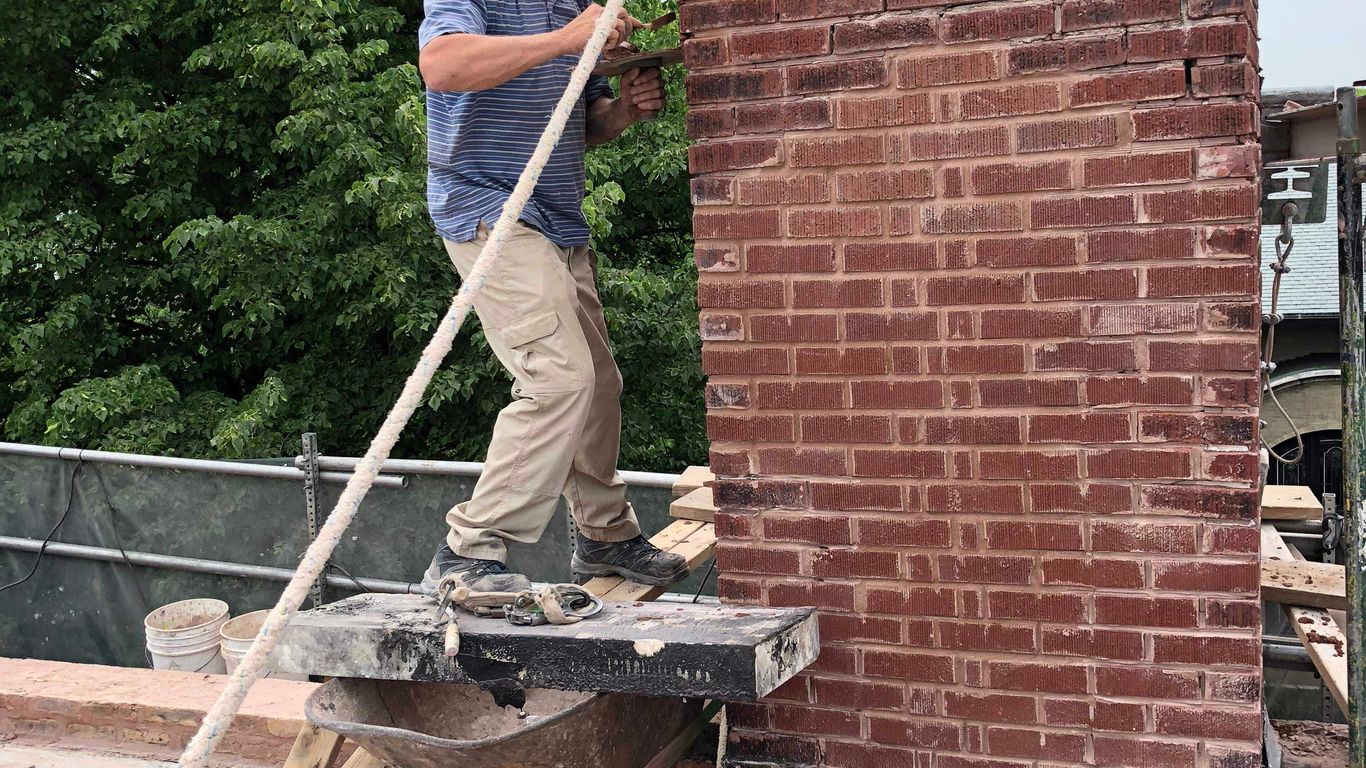 Person working on a brick chimney repair with tools and equipment.