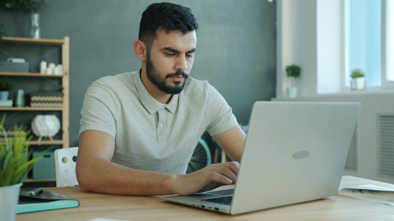 Hombre escribiendo en un portátil en un escritorio.