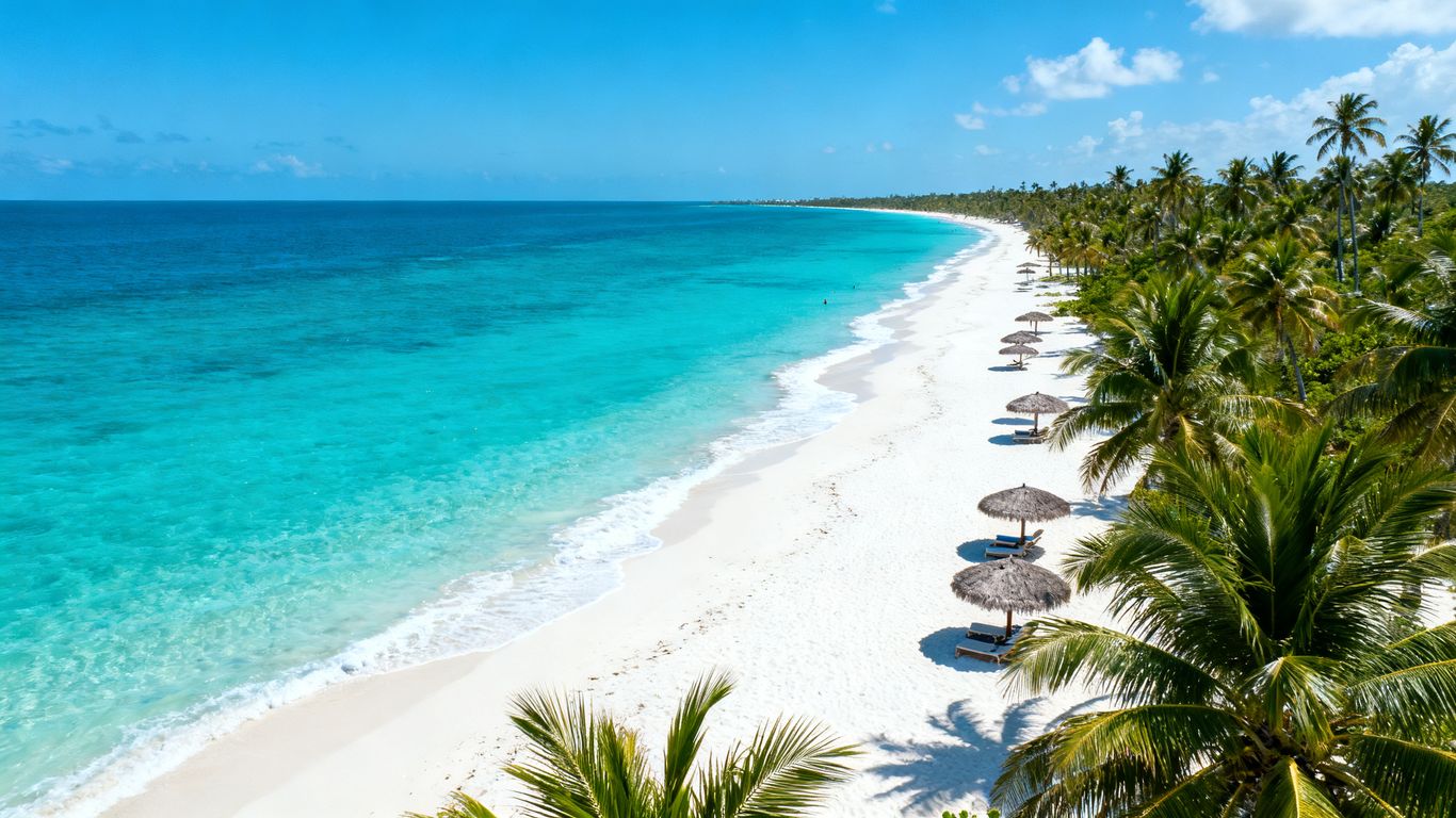 Calm turquoise waters and white sand beach with palm trees.
