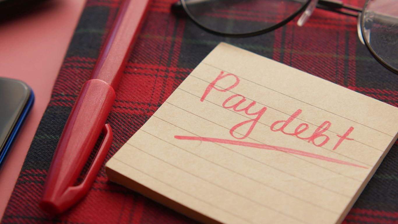 a note that says pay debt next to a pen and glasses