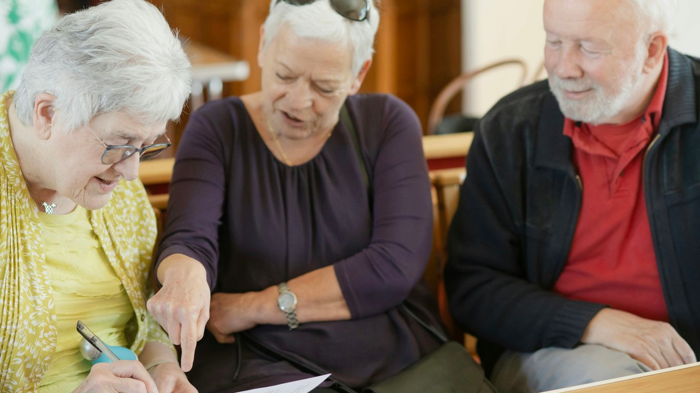 Three older adults are looking at a paper.