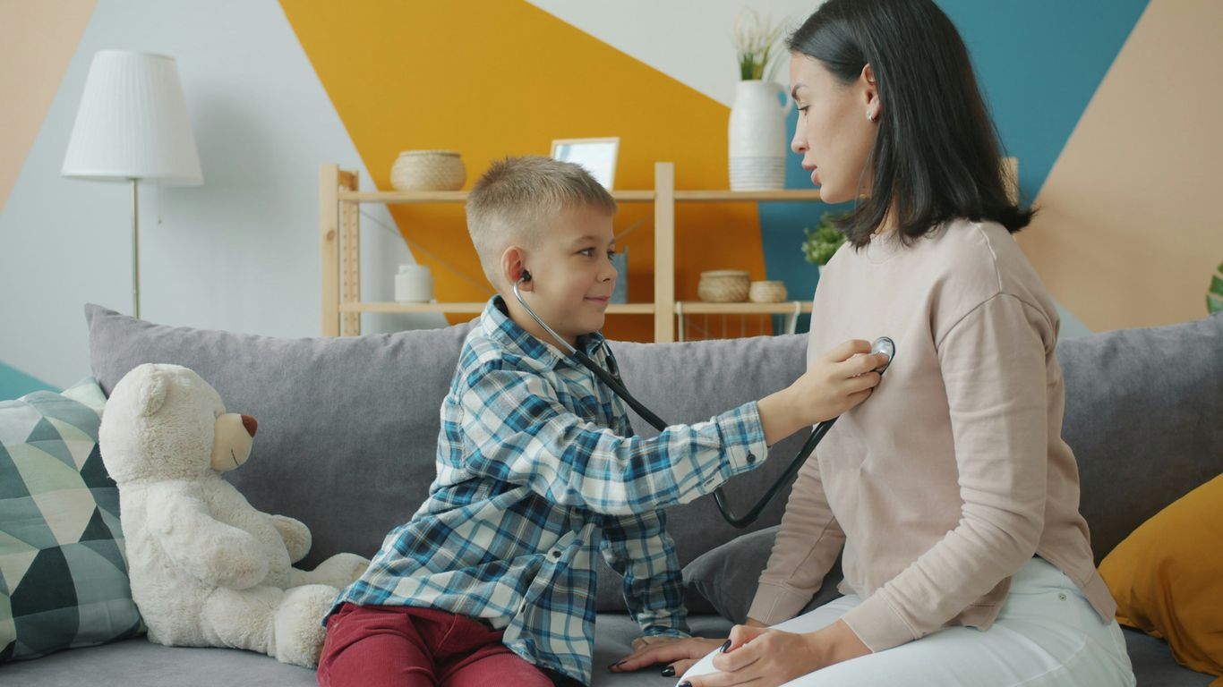 Boy uses stethoscope to listen to mother's chest.