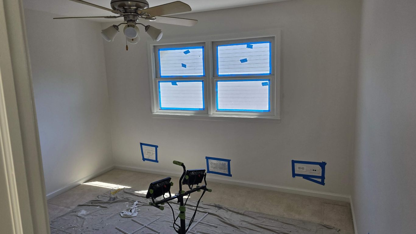 Room being renovated with taped windows and drop cloths.