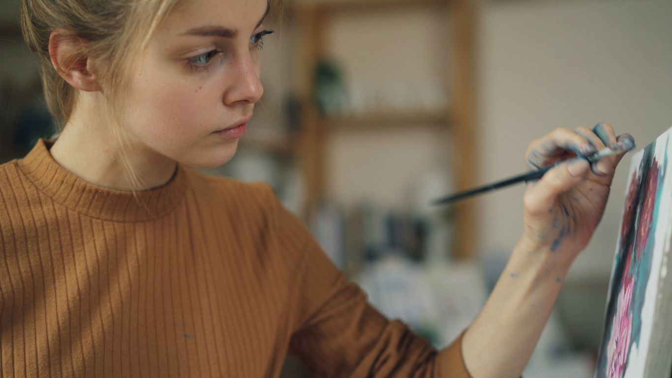 Young woman carefully paints on a canvas.