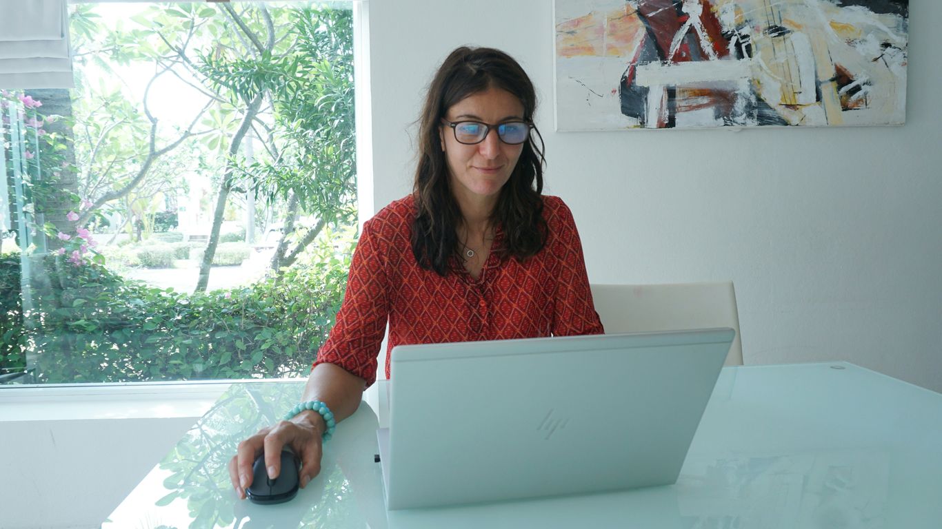 Woman works on laptop at a bright table.