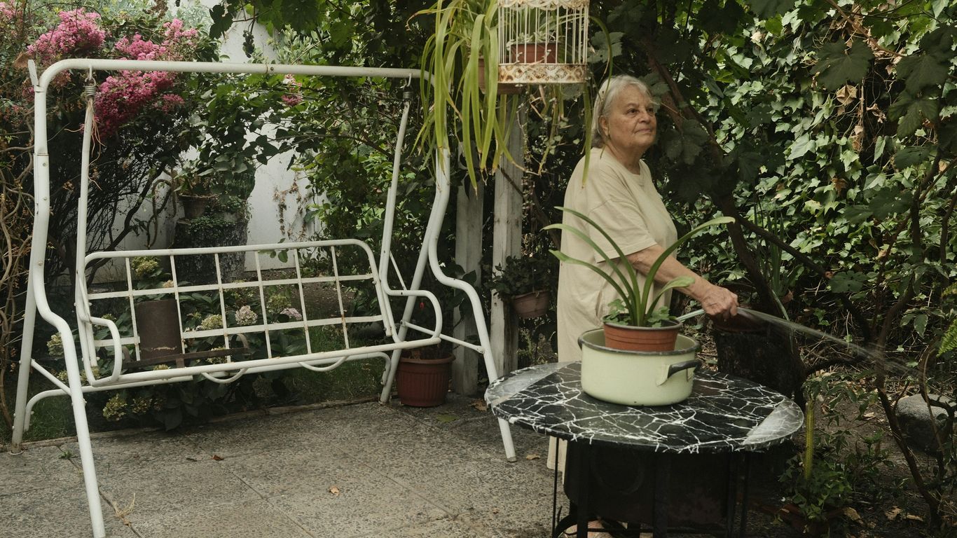 Elderly woman watering plants in a lush garden.
