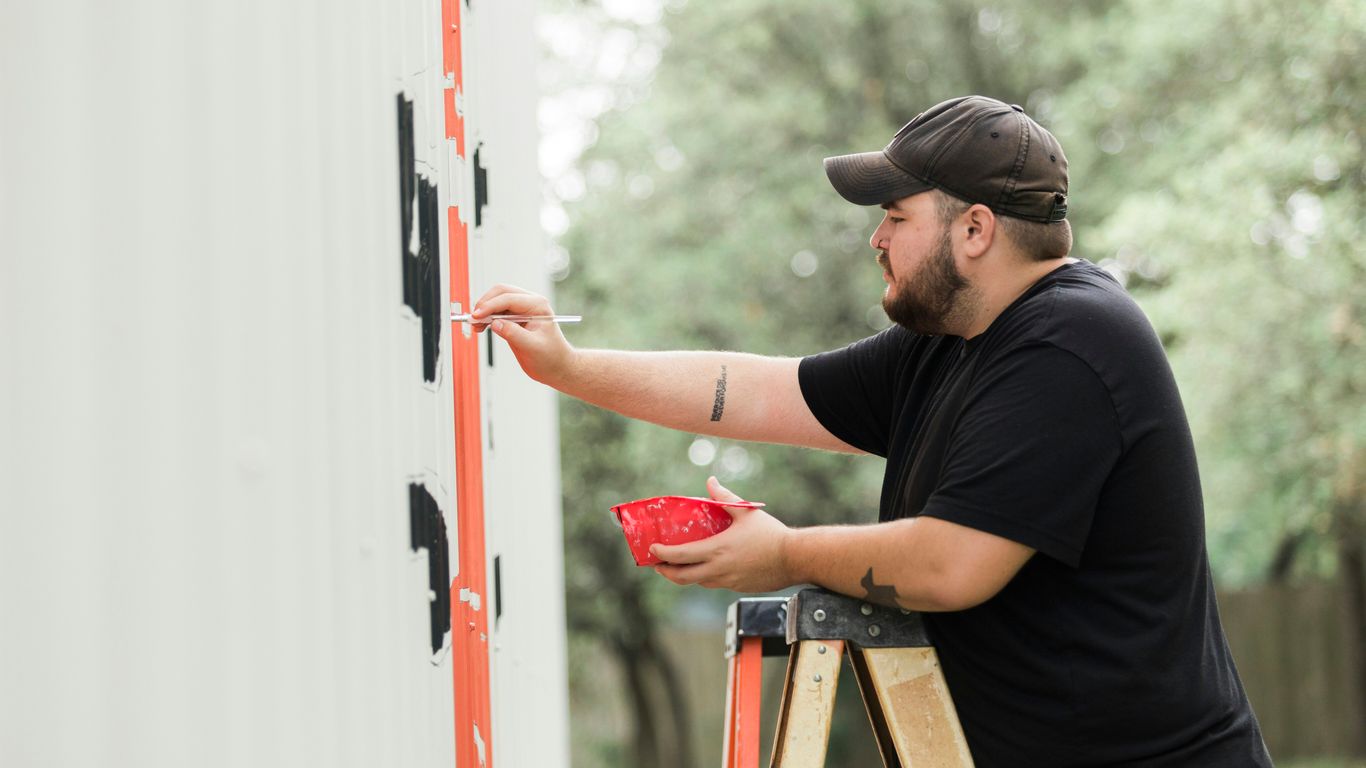 man in black shirt and black cap holding red and white wooden door during daytime