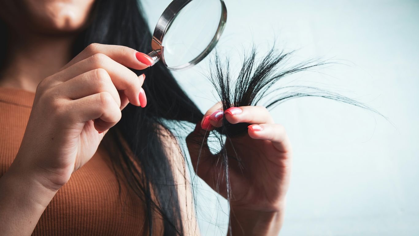 Woman examining split ends of hair with magnifying glass