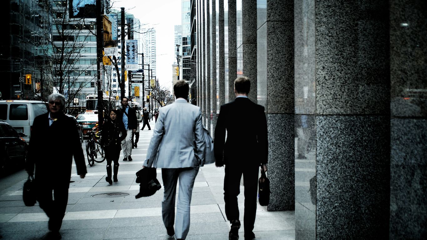 people walking on sidewalk pathway beside road with vehicles and high-rise buildings during daytime