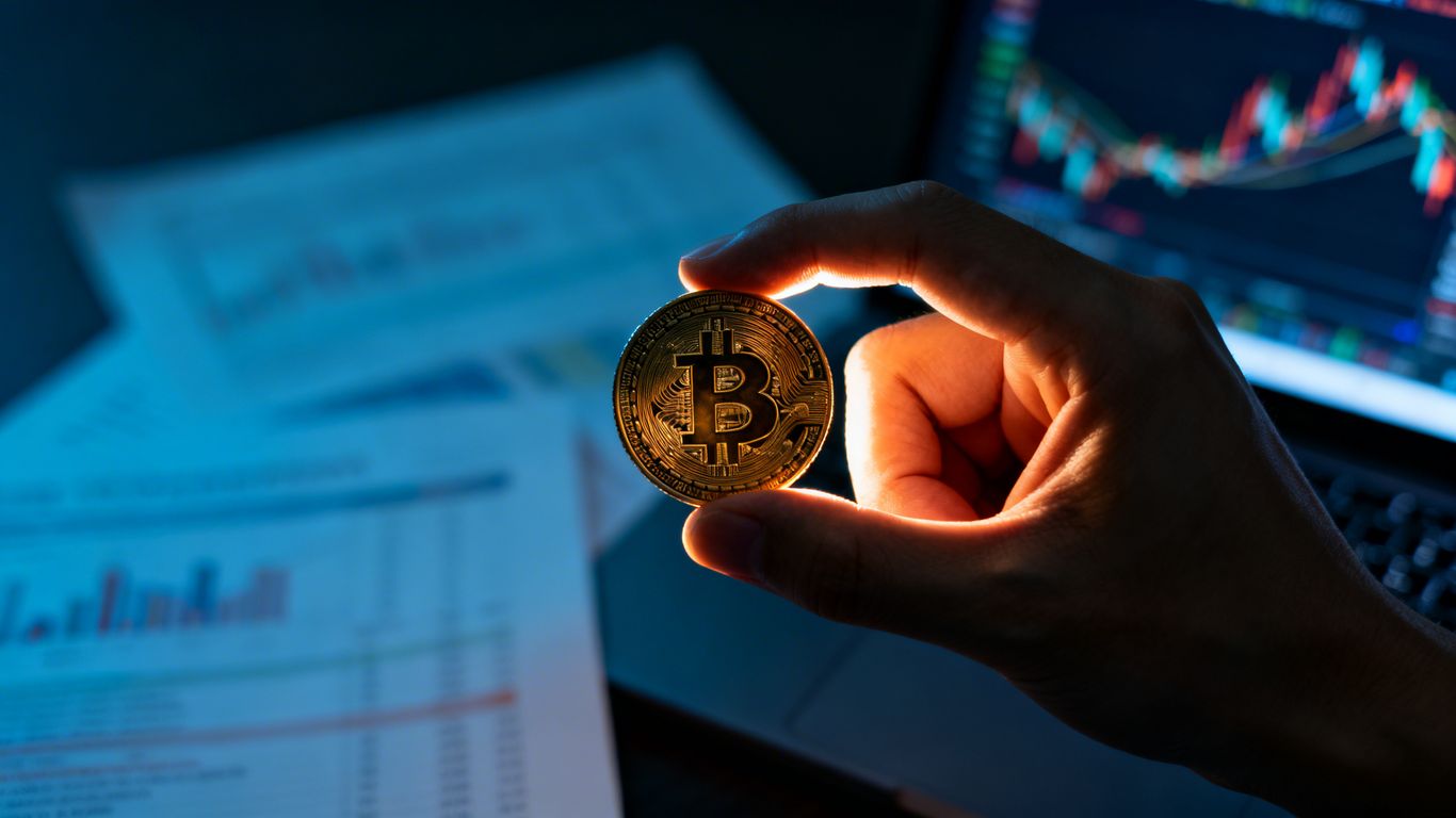 Digital currency coin held in hand, financial charts in background.