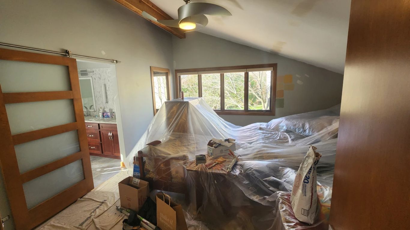 Bedroom covered in plastic sheeting for painting, with supplies visible.