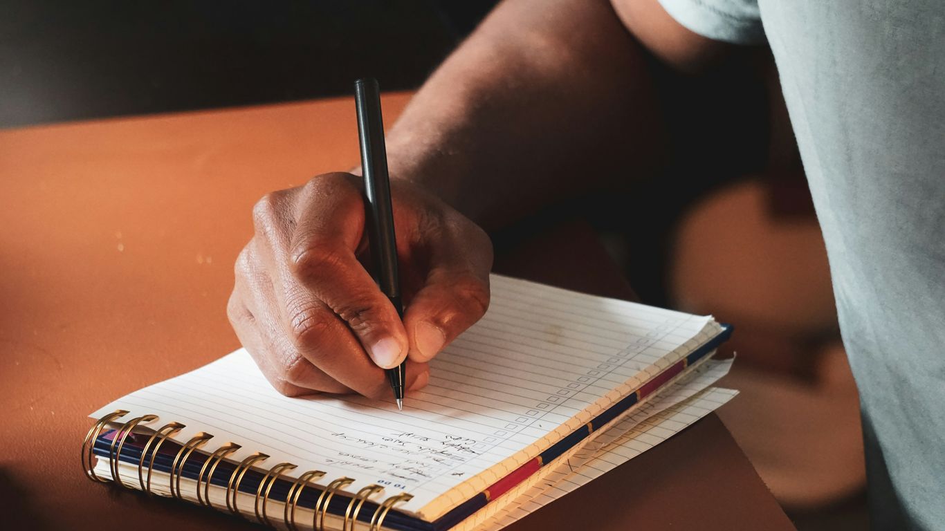 a person writing on a notebook with a pen