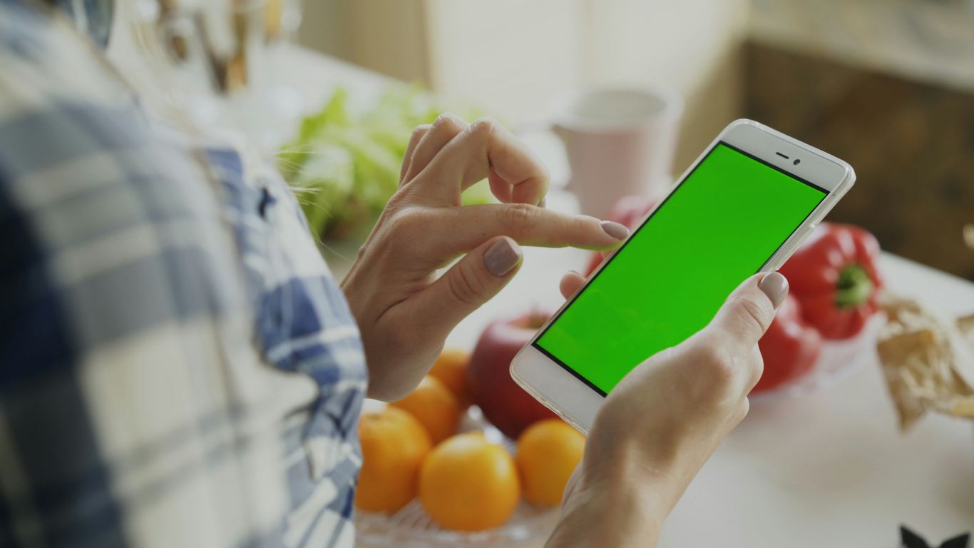 Person using a smartphone with a green screen.