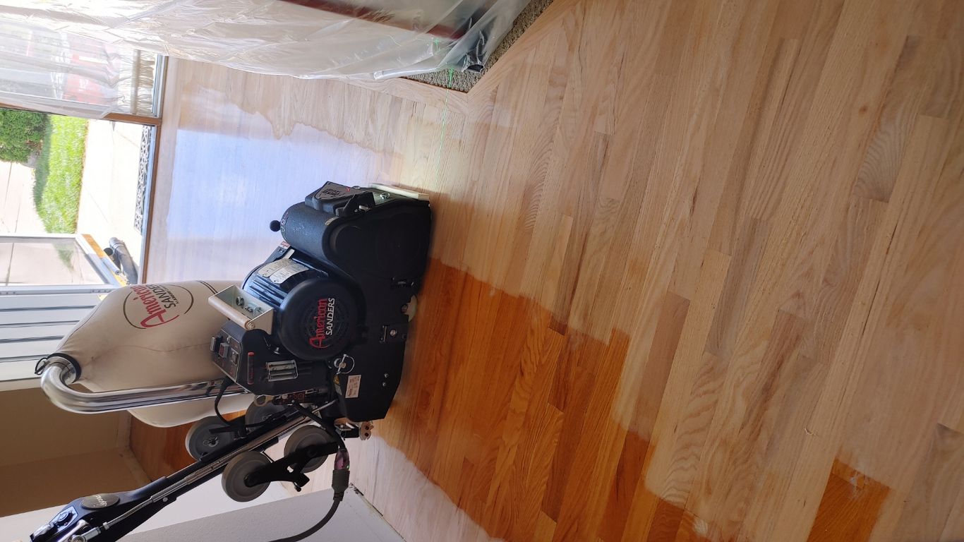 Floor refinishing equipment in a partially finished wooden floor area.
