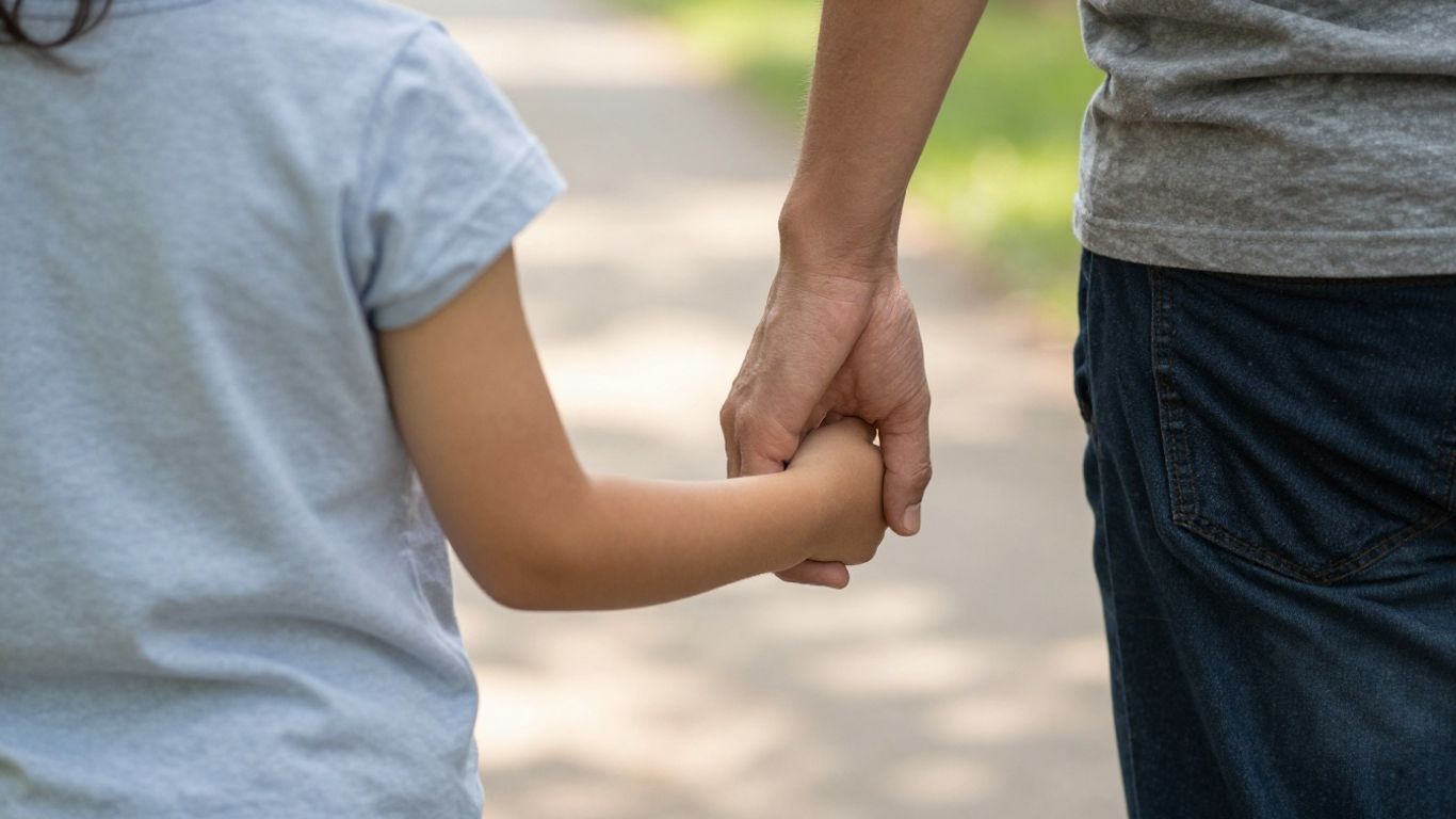 Parent and child walking hand-in-hand on a sunny path.