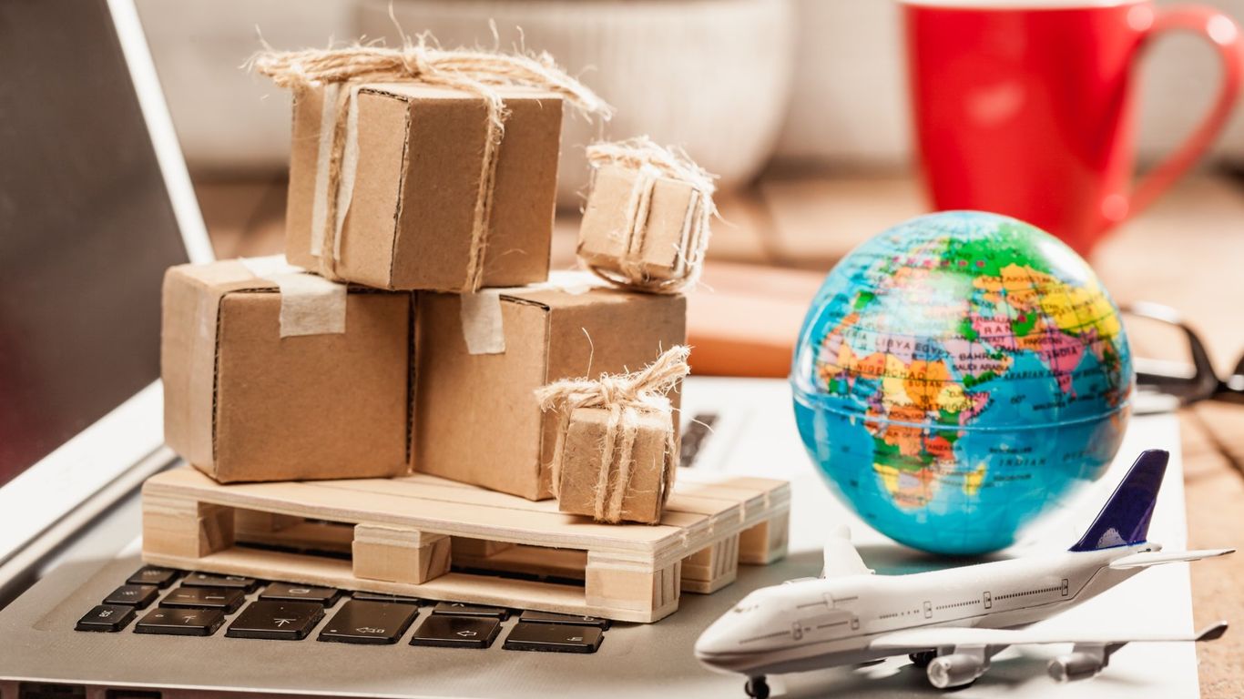 Cardboard boxes on a pallet on a laptop with a globe and airplane.