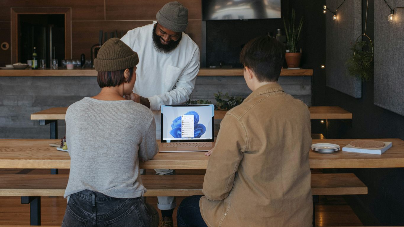 Three people sitting on benches at work around a Microsoft laptop