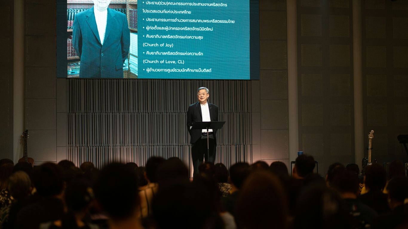 Man in suit speaks at podium in front of audience.