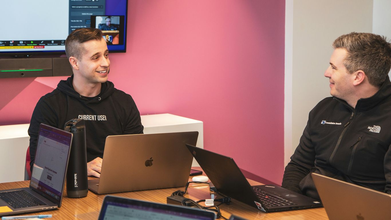 a couple of men sitting at a table with laptops