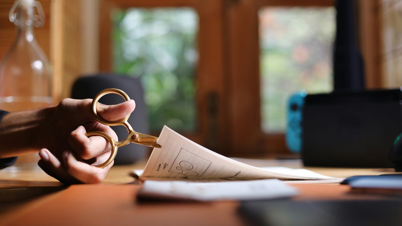 a person holding a pair of scissors over a piece of paper