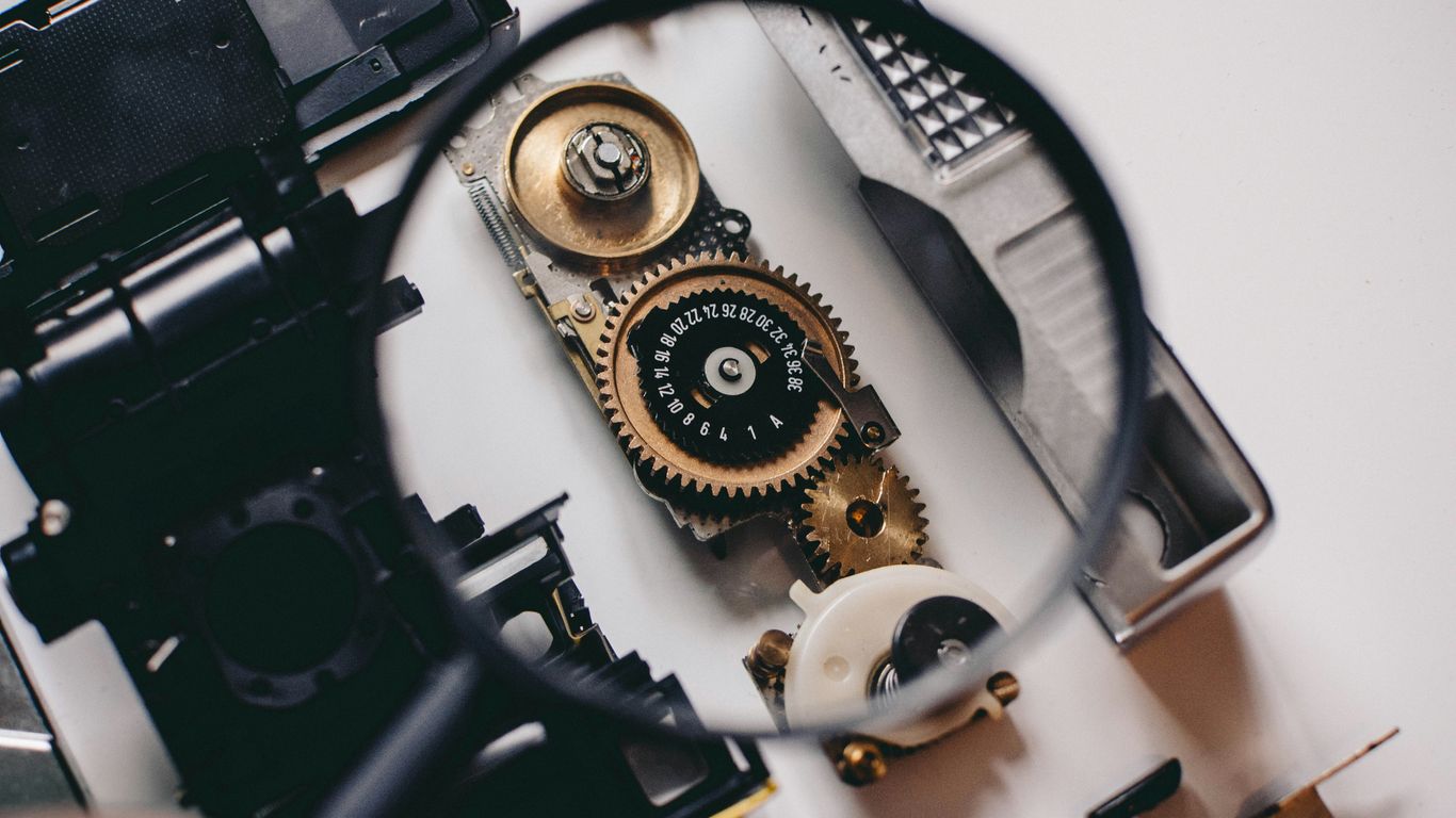 person using magnifying glass to see gold and white device gear