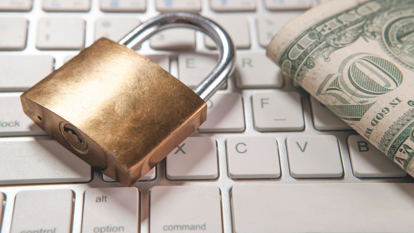 A padlock and dollar bills rest on a computer keyboard.