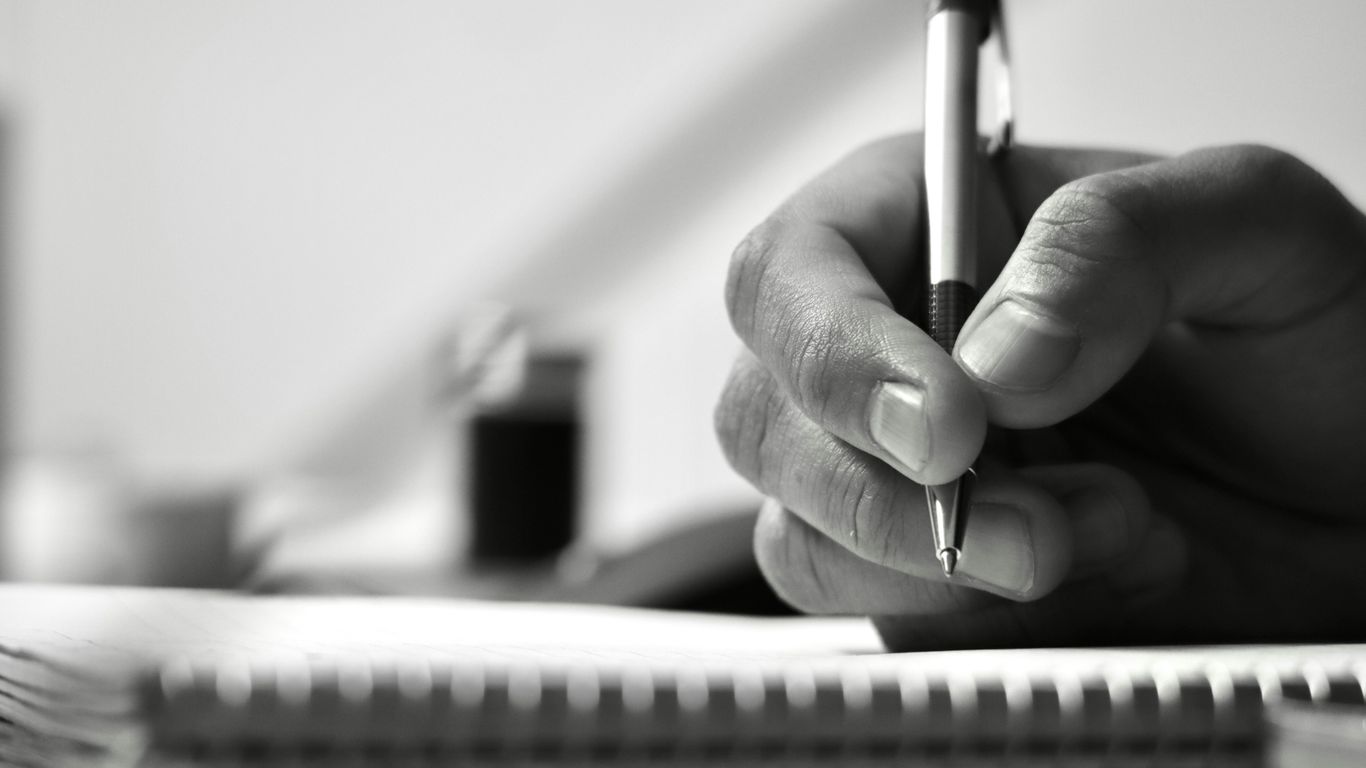 a person writing on a notebook with a pen