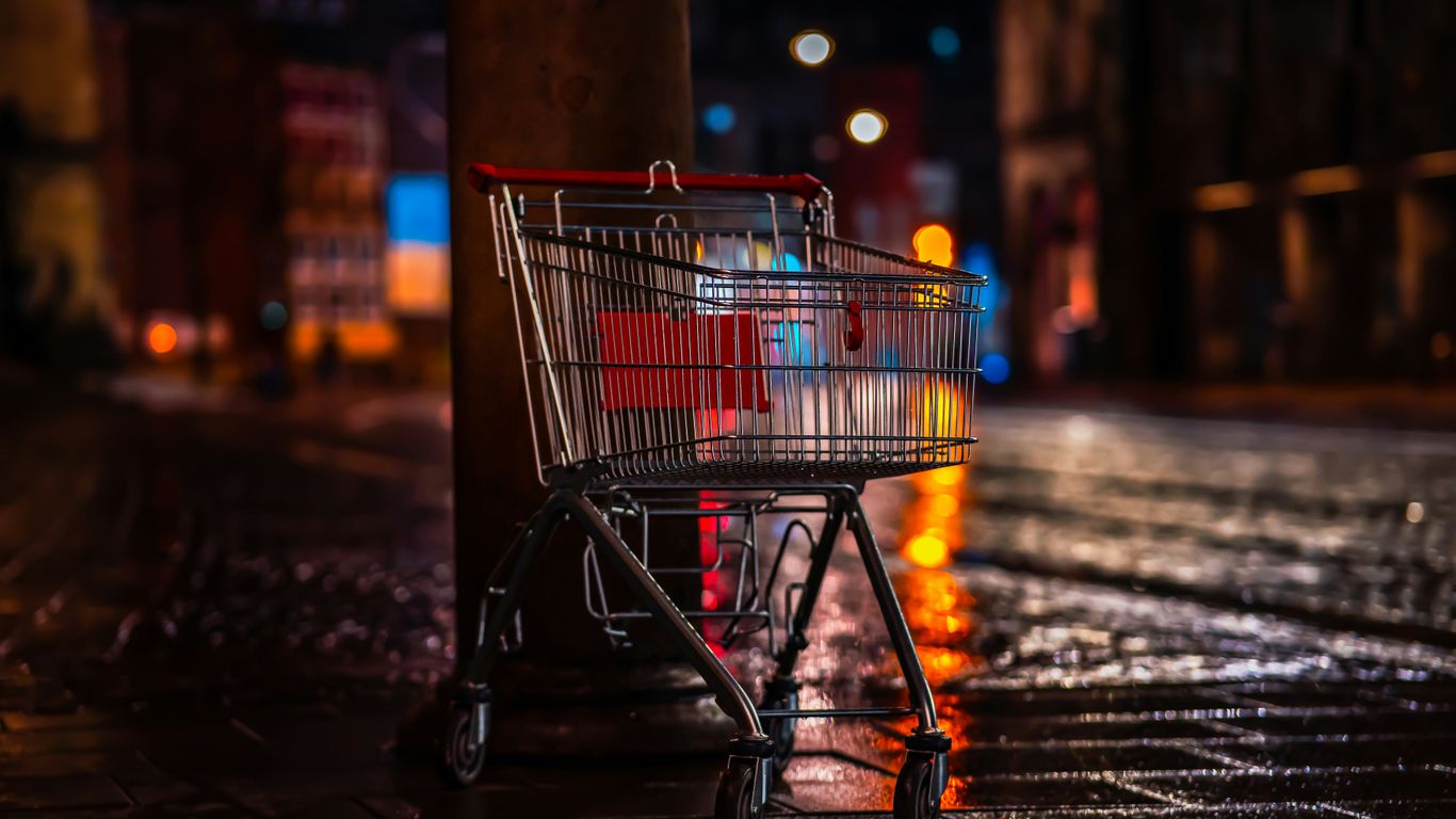 a shopping cart sitting next to a pole on a wet sidewalk