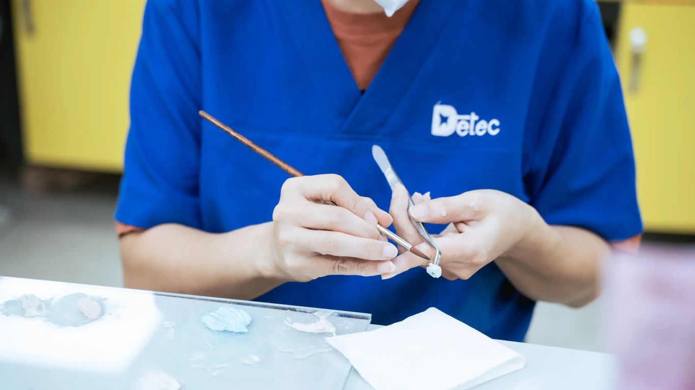 A person in a blue uniform works on a dental prosthetic.