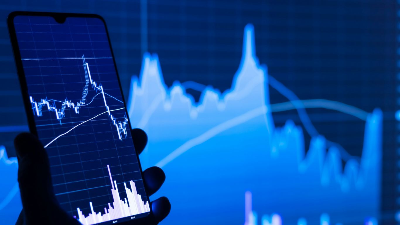 a person holding a cell phone in front of a stock chart