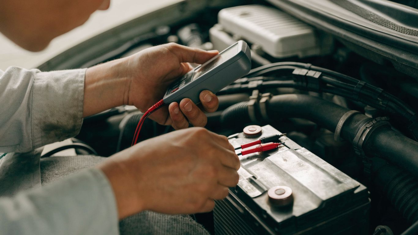 Photorealistic close-up of an automotive technician safely checking a car battery with a digital multimeter, tools arranged neatly, engine bay in soft daylight