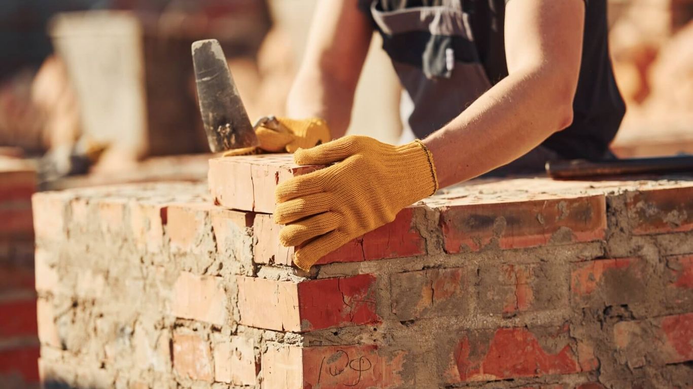 A person wearing gloves places a brick on a wall.