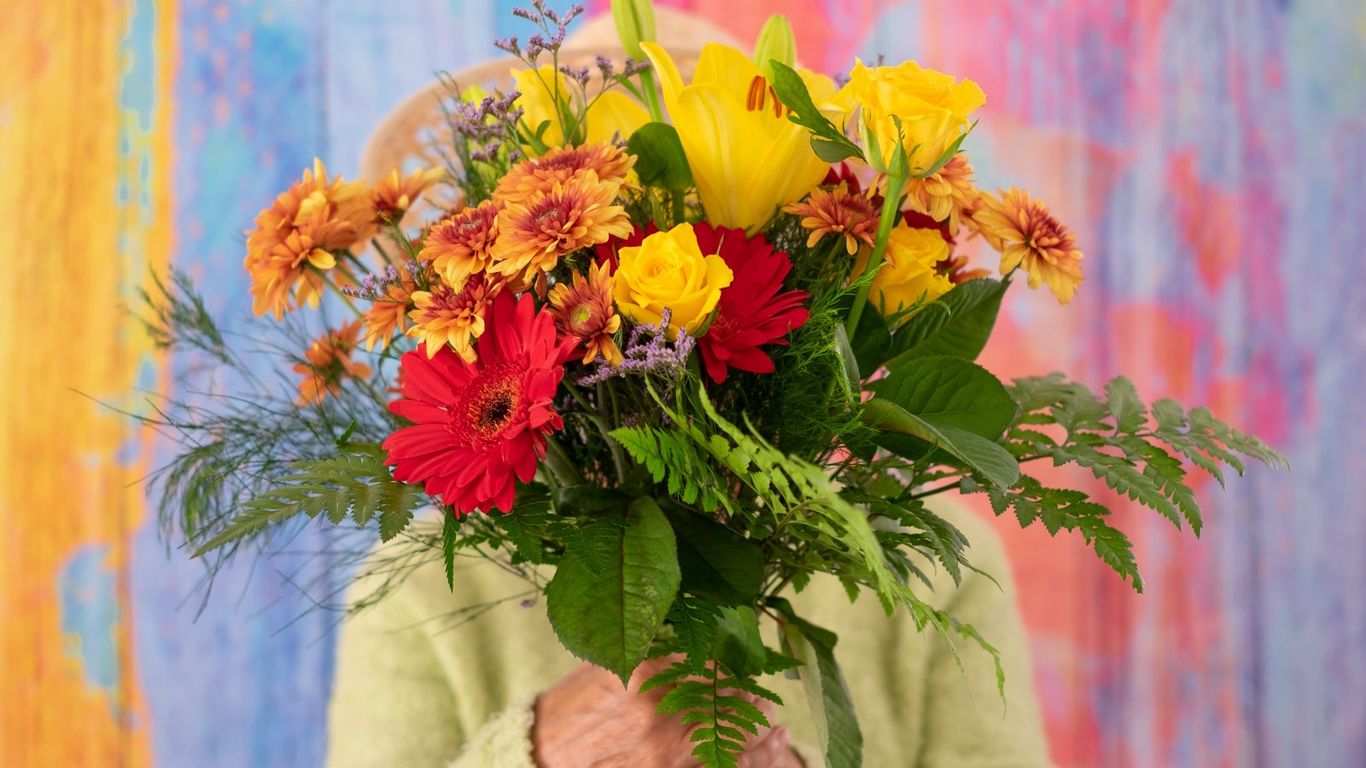A person holds a vibrant bouquet of yellow, red, and orange flowers.