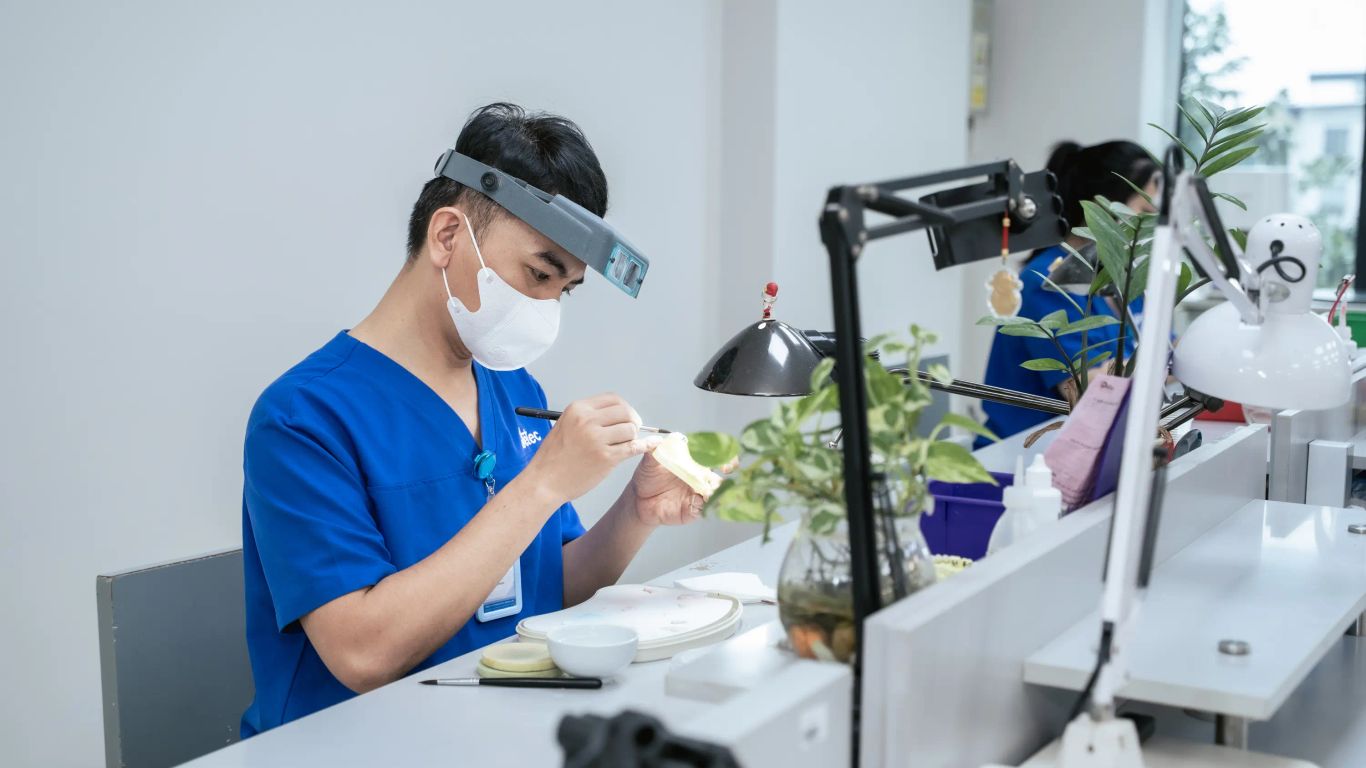 A person works on a dental prosthesis with magnification and tools.