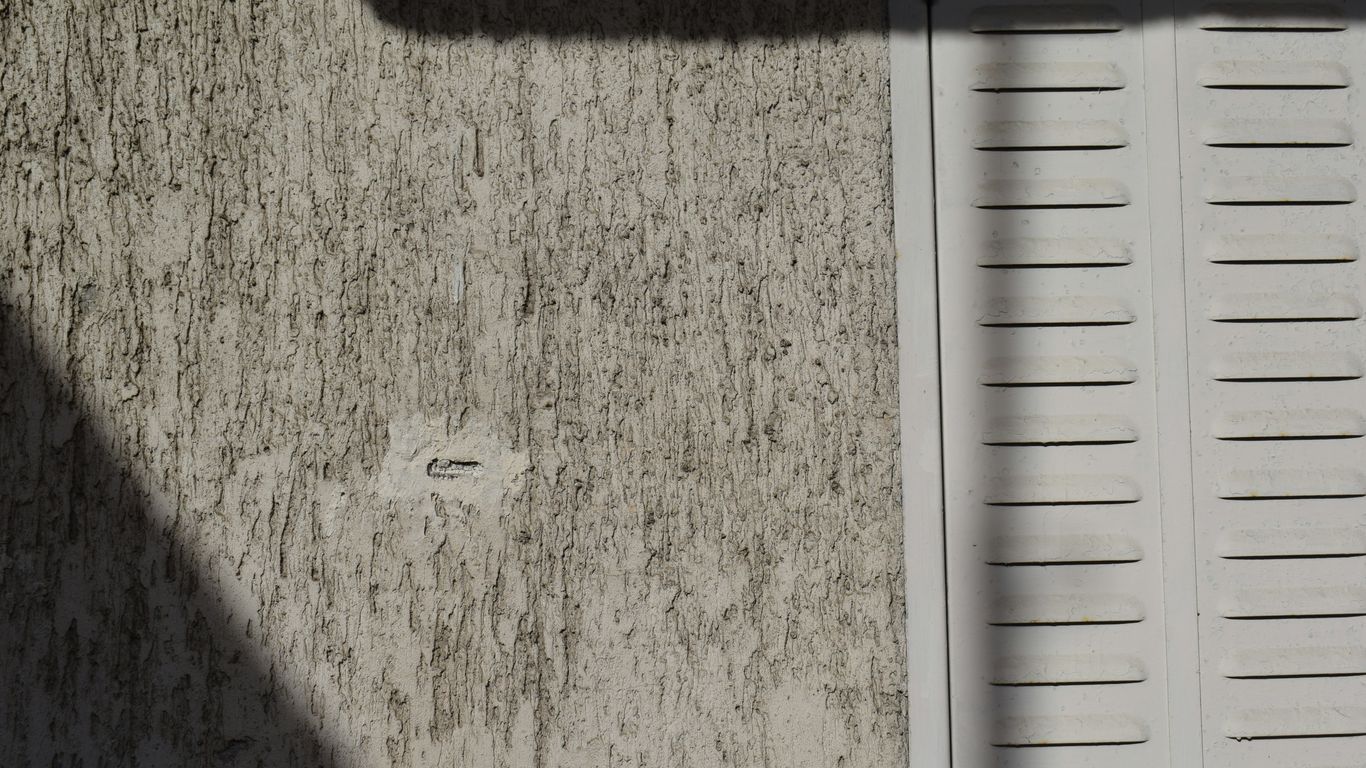 Textured wall with white shutter and shadows.