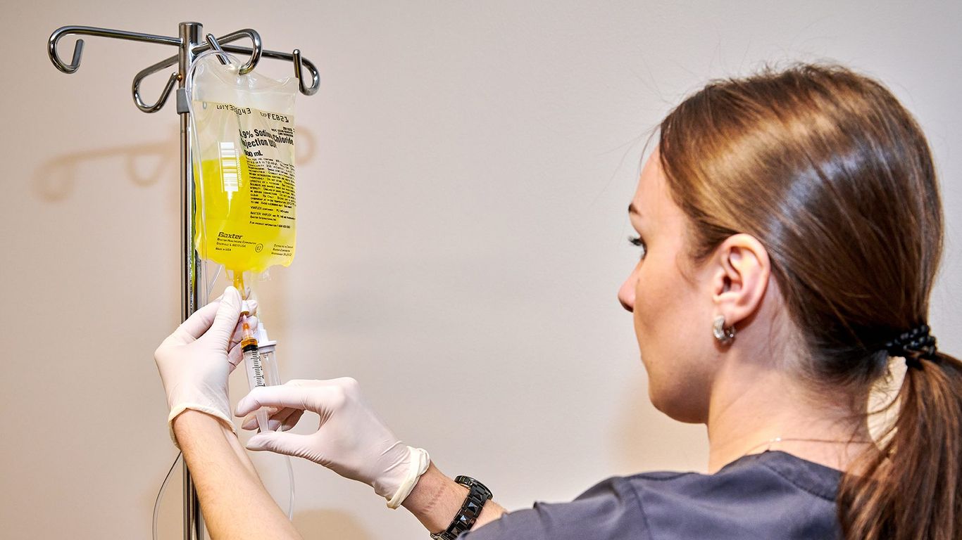 A person prepares an IV bag and syringe for medical treatment.