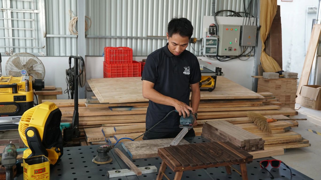 A person sands a wooden object in a workshop with lumber.