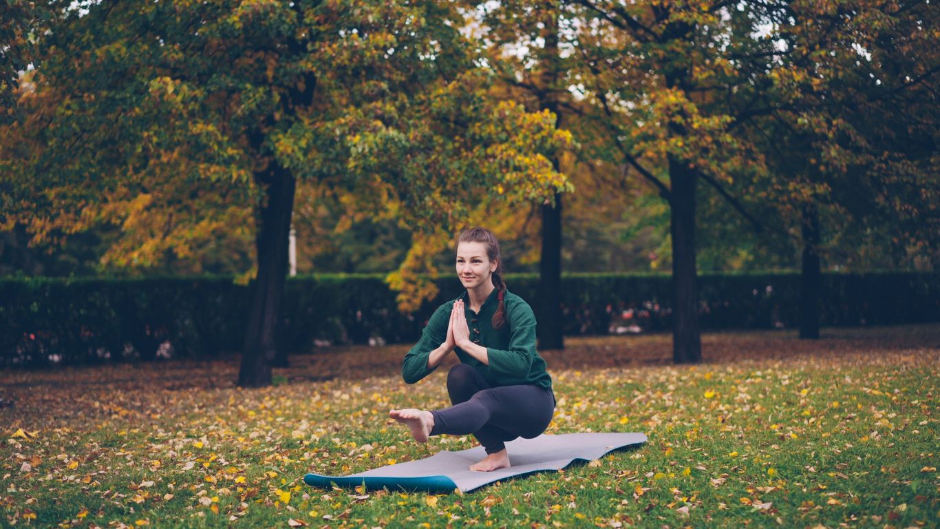Woman practicing yoga on a mat in autumn park.