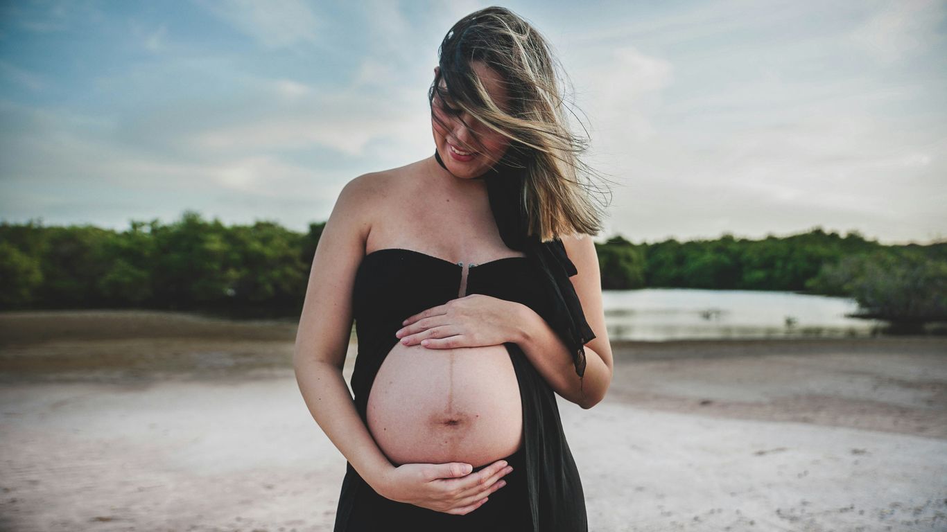 Pregnant woman in black dress touching her belly