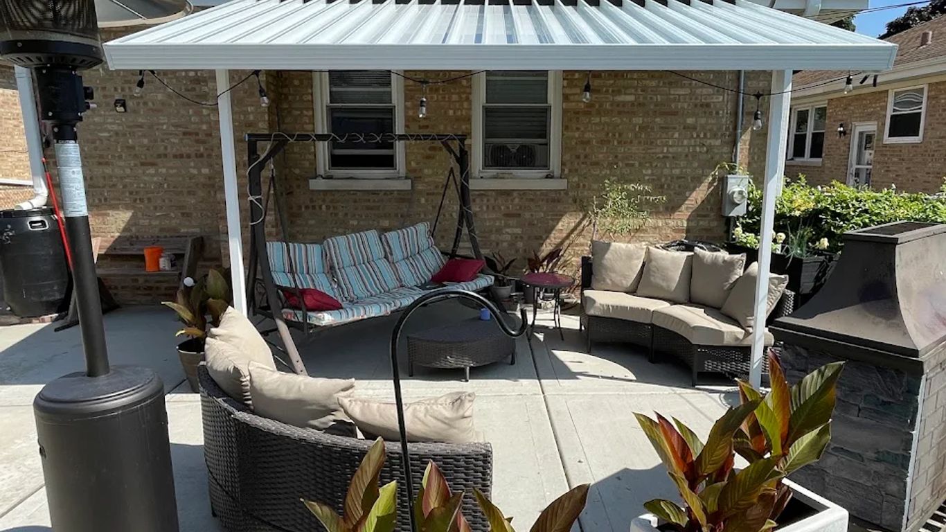 Patio with covered seating, swing, heater, and plants.