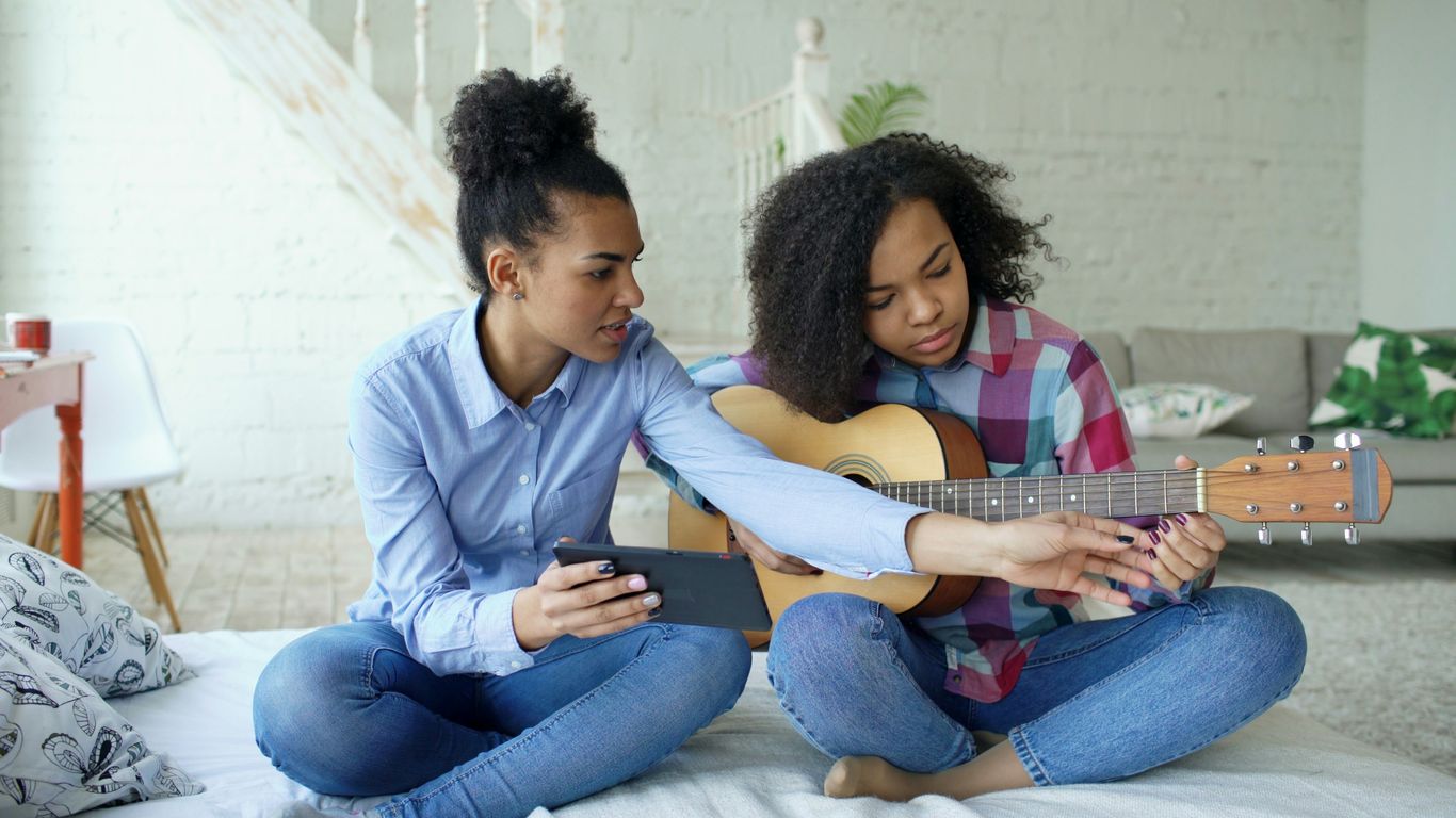 Two girls learning to play guitar together indoors.