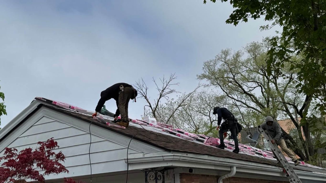 Workers on a roof installing new shingles on a cloudy day.