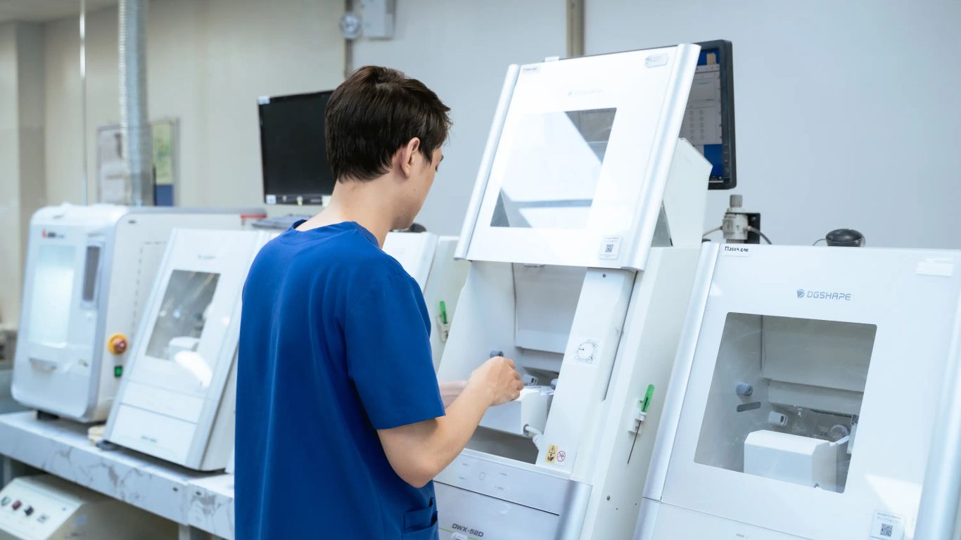 A person in blue scrubs works with advanced dental milling machines.
